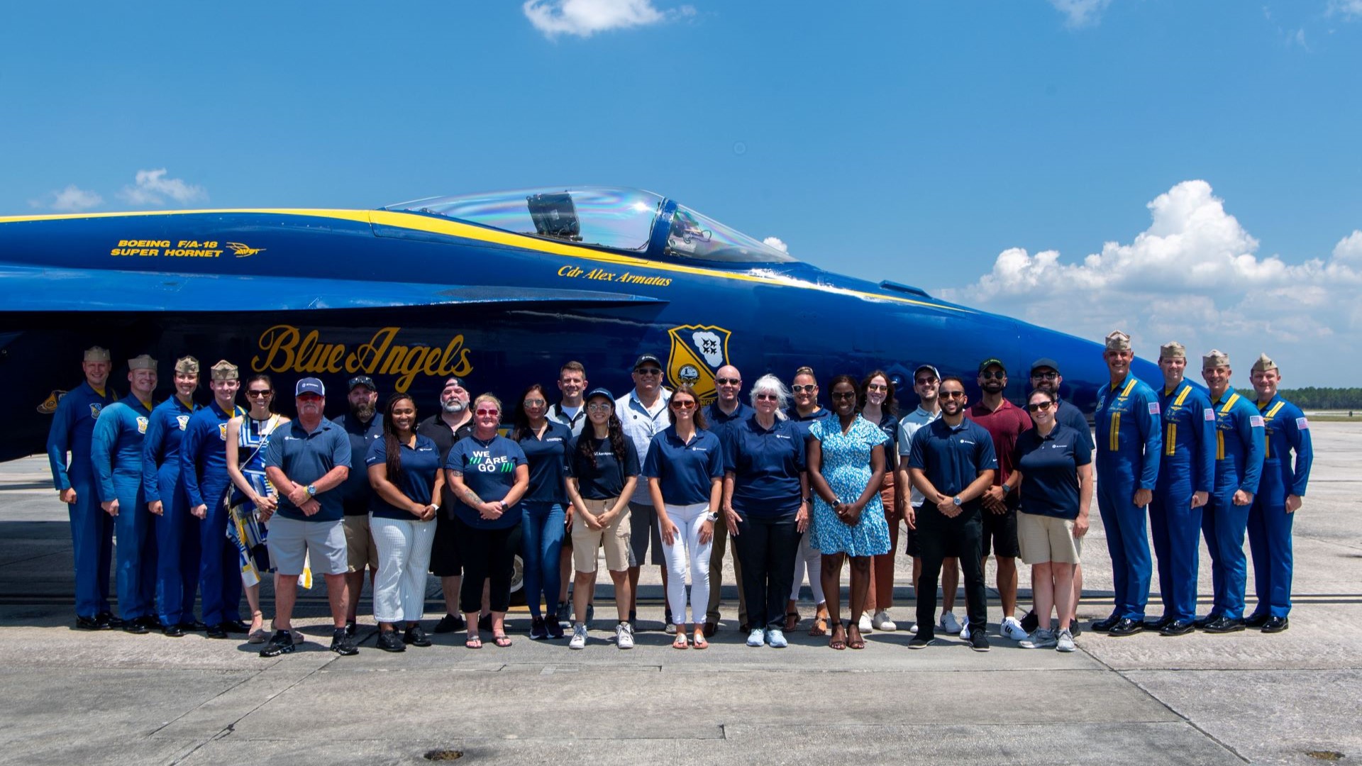 19 people standing in front of a Blue Angel jet